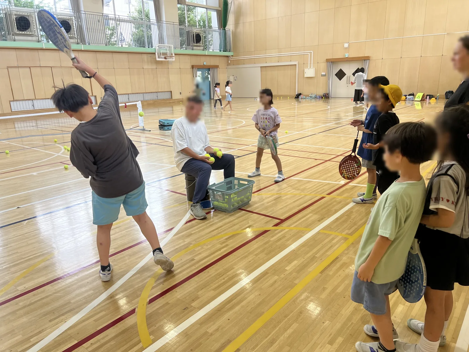 香取小学校の体育館で、パドルを持った子どもたちがコーチの球出し練習に並んでいる様子